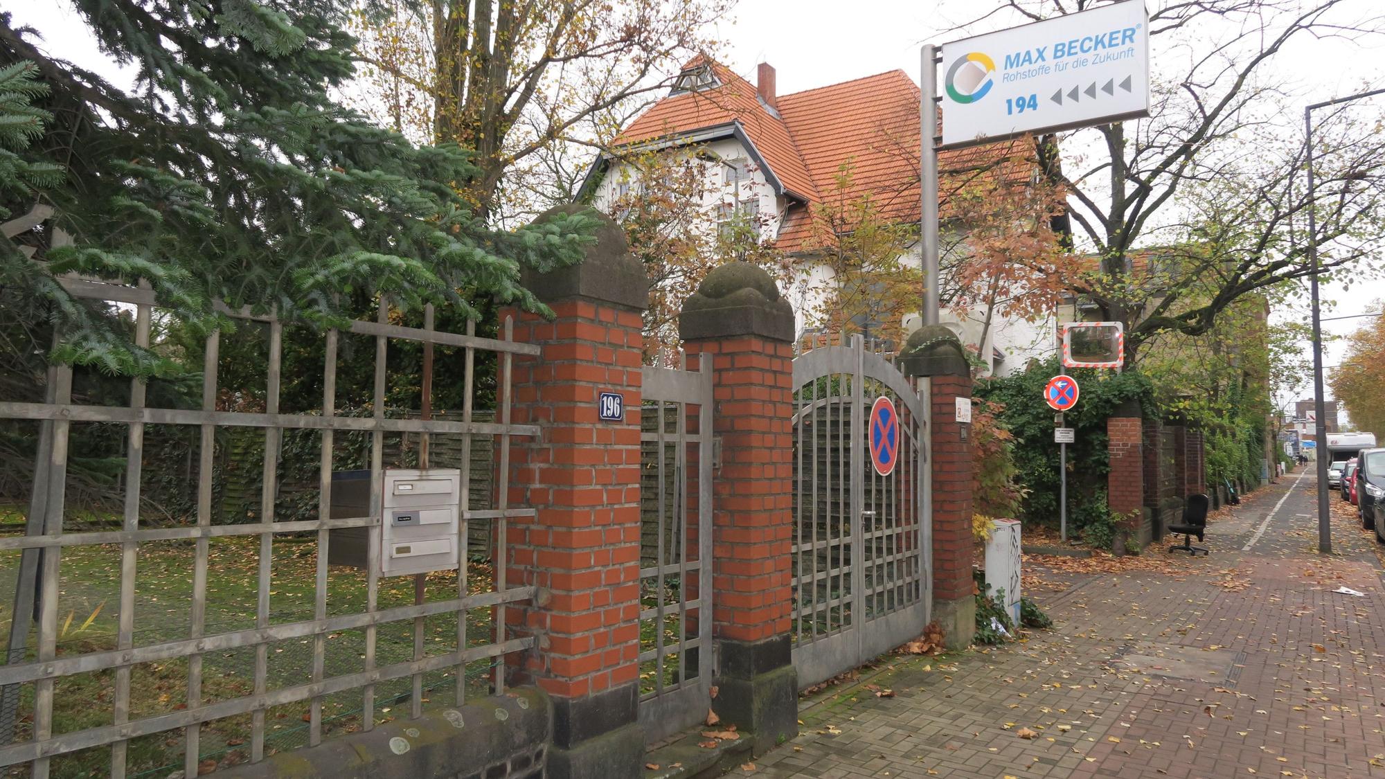 Ein Schild oberhalb eines Zauns weist auf das Unternehmen Max Becker hin. Im Hintergrund ist eine Gründerzeit-Villa zu sehen.