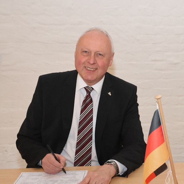 Portraitfoto von Gero Karthaus, er schaut direkt in die Kamera und trägt einen dunklen Anzug, weißes Hemd und Krawatte.