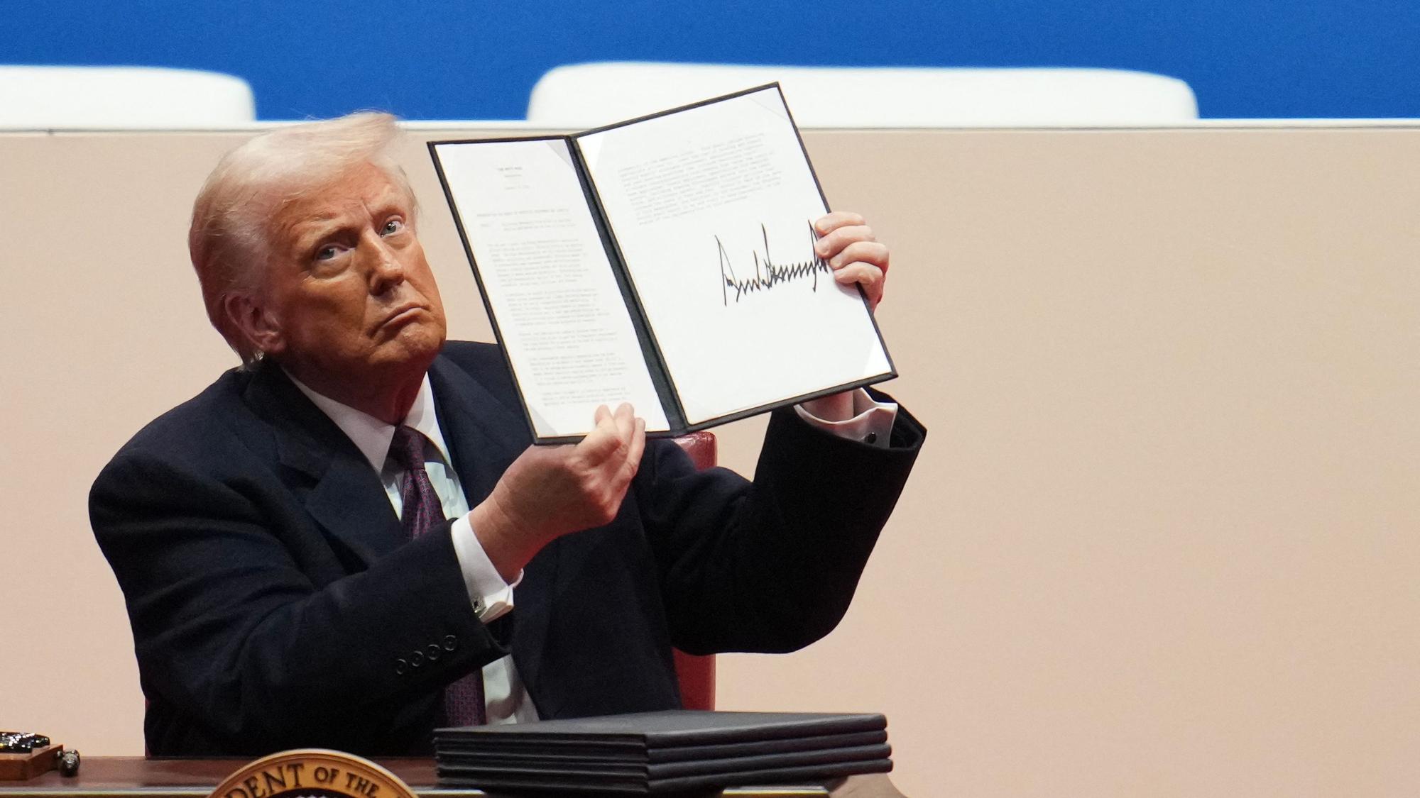 Donald Trump hält ein Dekret mit seiner Unterschrift in die Höhe.