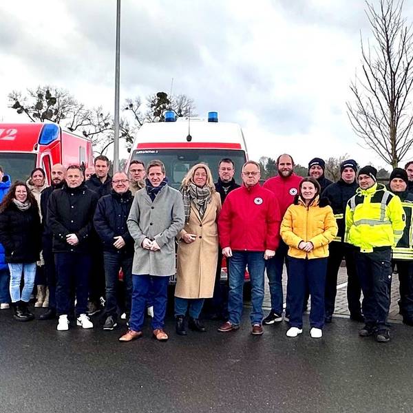 Eine große Gruppe Menschen steht vor drei Einsatzfahrzeugen der Rettungswache.