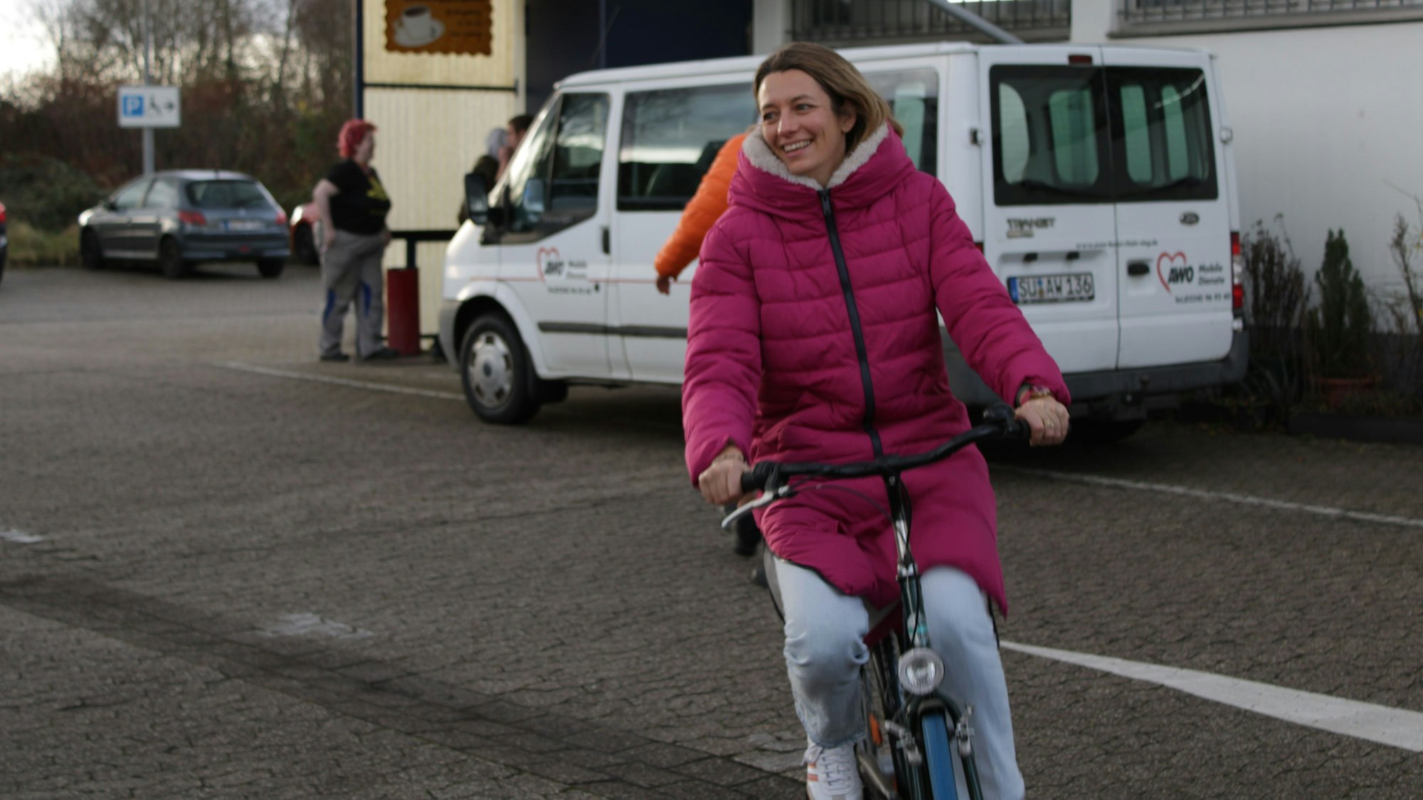 Eine junge Frau in Daunenjacke sitzt lächelnd auf einem Fahrrad.