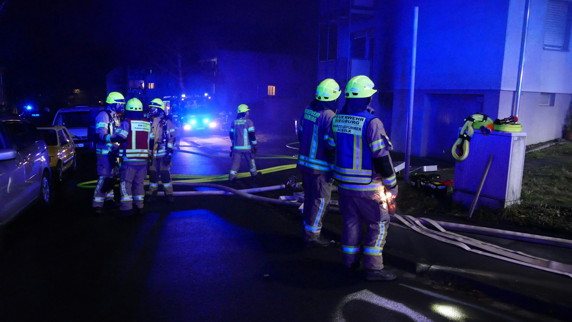 Feuerwehrleute stehen vor einem Haus, aus dem Qualm dringt.