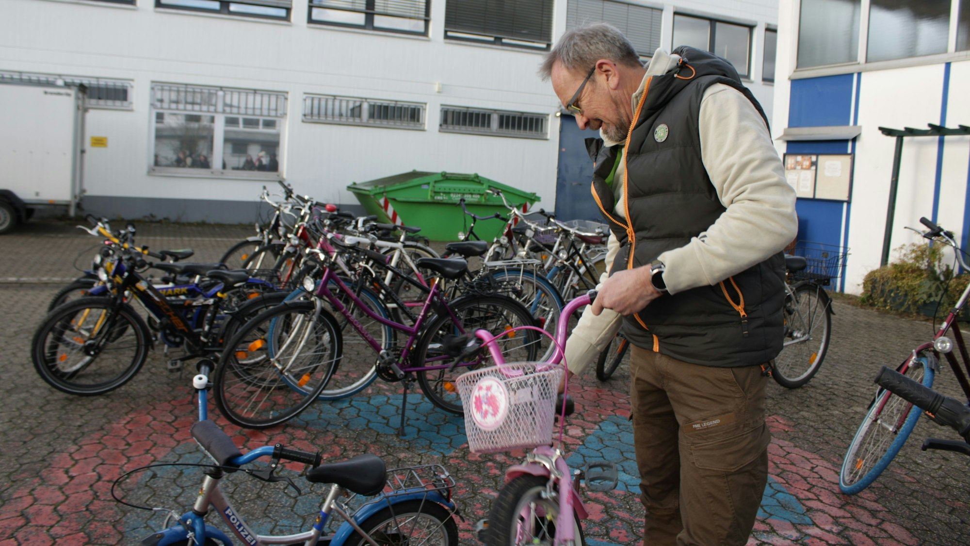 Ein Mann hebt ein rosafarbenes Kinderfahrrad hoch, im Hintergrund sind weitere Fahrräder zu sehen.