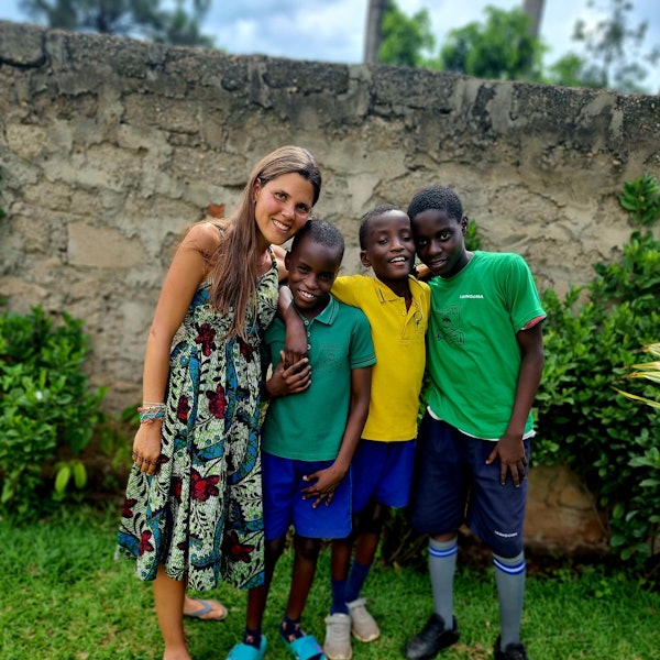 Eine junge Frau steht mit drei Kindern vor einer Wand. Die vier Personen lächeln in die Kamera.