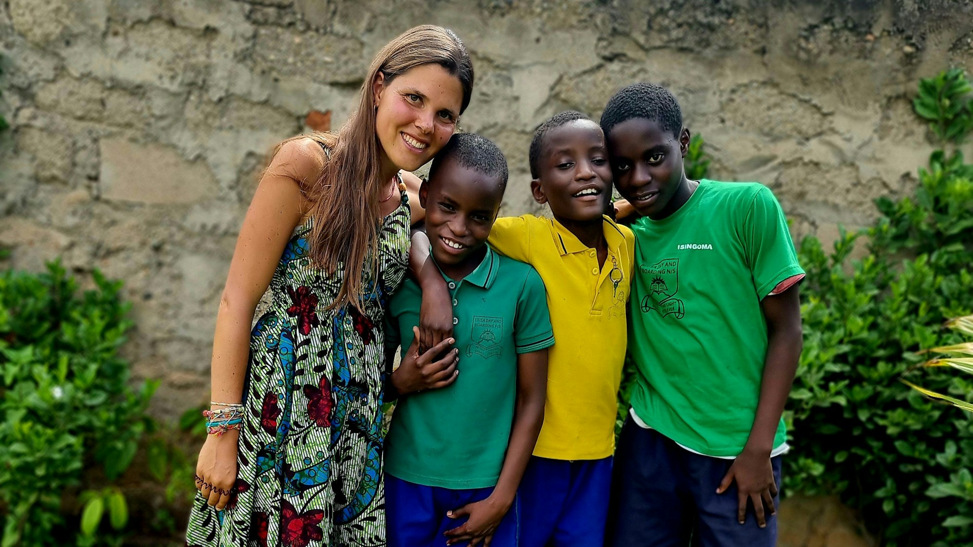 Eine junge Frau steht mit drei Kindern vor einer Wand. Die vier Personen lächeln in die Kamera.