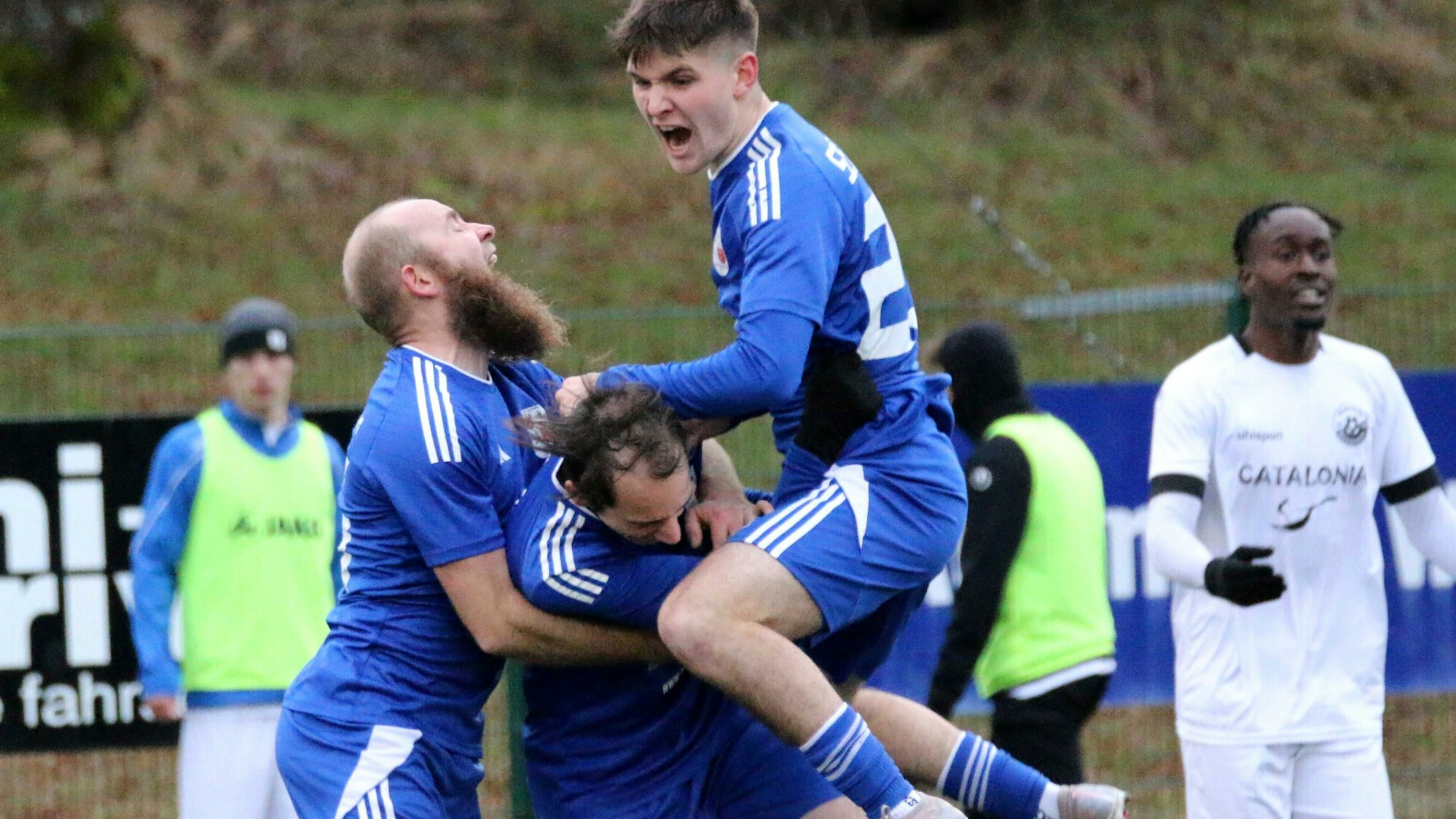 Drei Spieler der SG Dahlem-Schmidtheim in blauen Trikots jubeln.