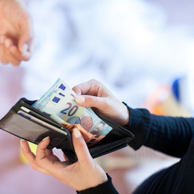 Eine Person zieht 20-Euro-Scheine aus ihrem Portemonnaie, um sie einer anderen Person zu geben.