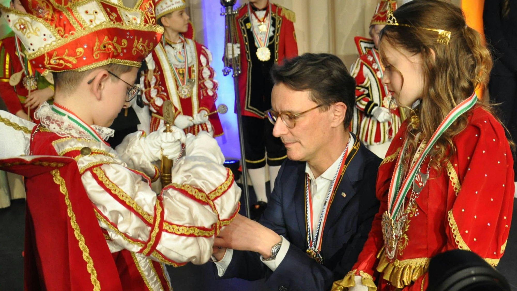 Ministerpräsident Hendrik Wüst kniet vor dem Kinderprinzen aus Kall, der ihm einen Orden umhängt.
