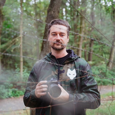 Ein Mann mit Kamera steht hinter einem Zaun.