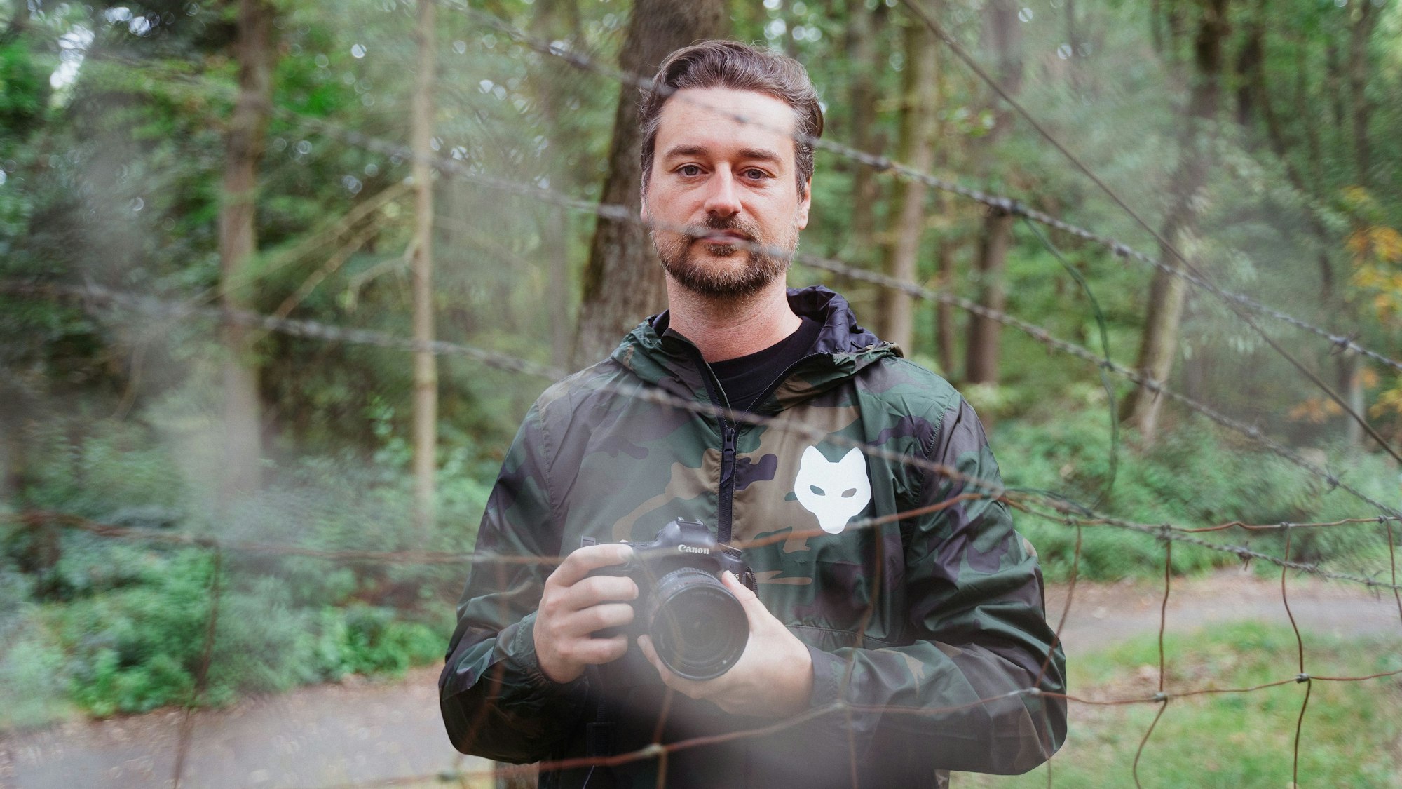 Ein Mann mit Kamera steht hinter einem Zaun.