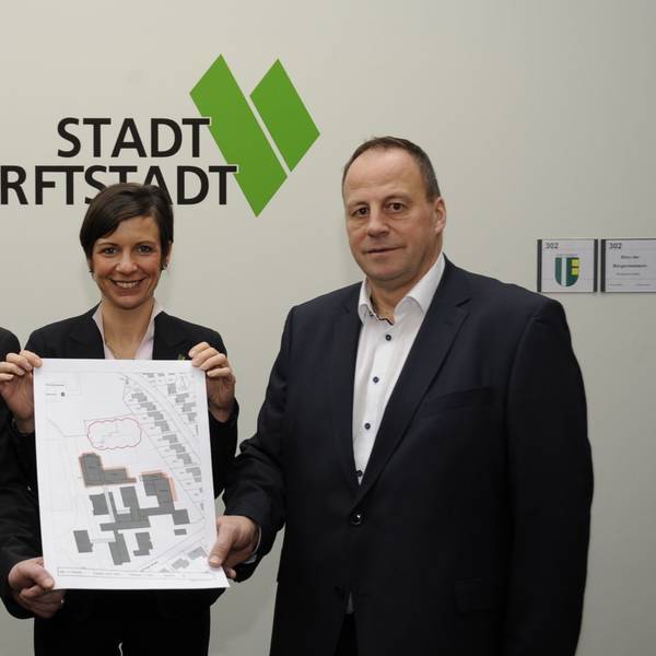 Drei Menschen stehen vor einer Wand und halten einen Plan.