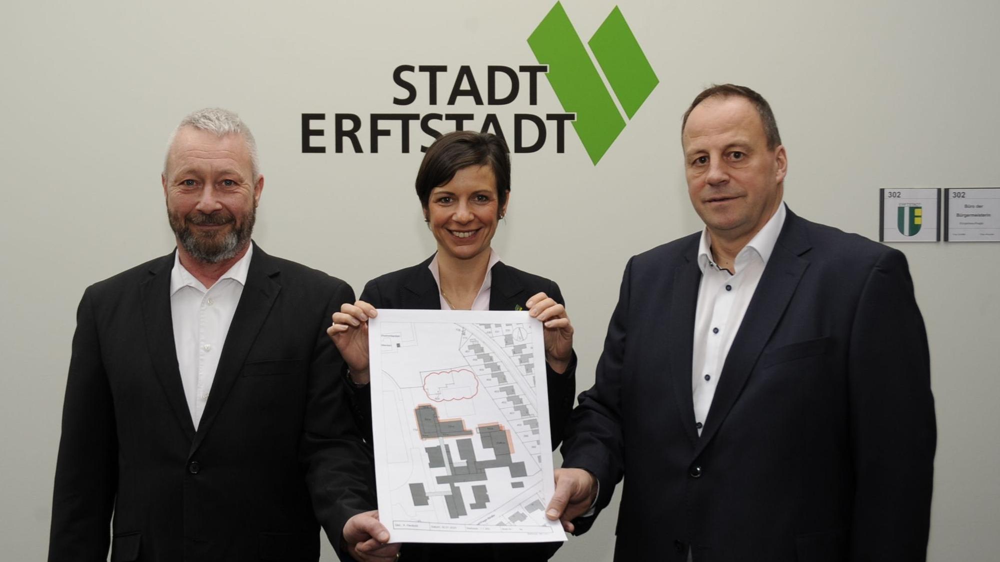 Drei Menschen stehen vor einer Wand und halten einen Plan.