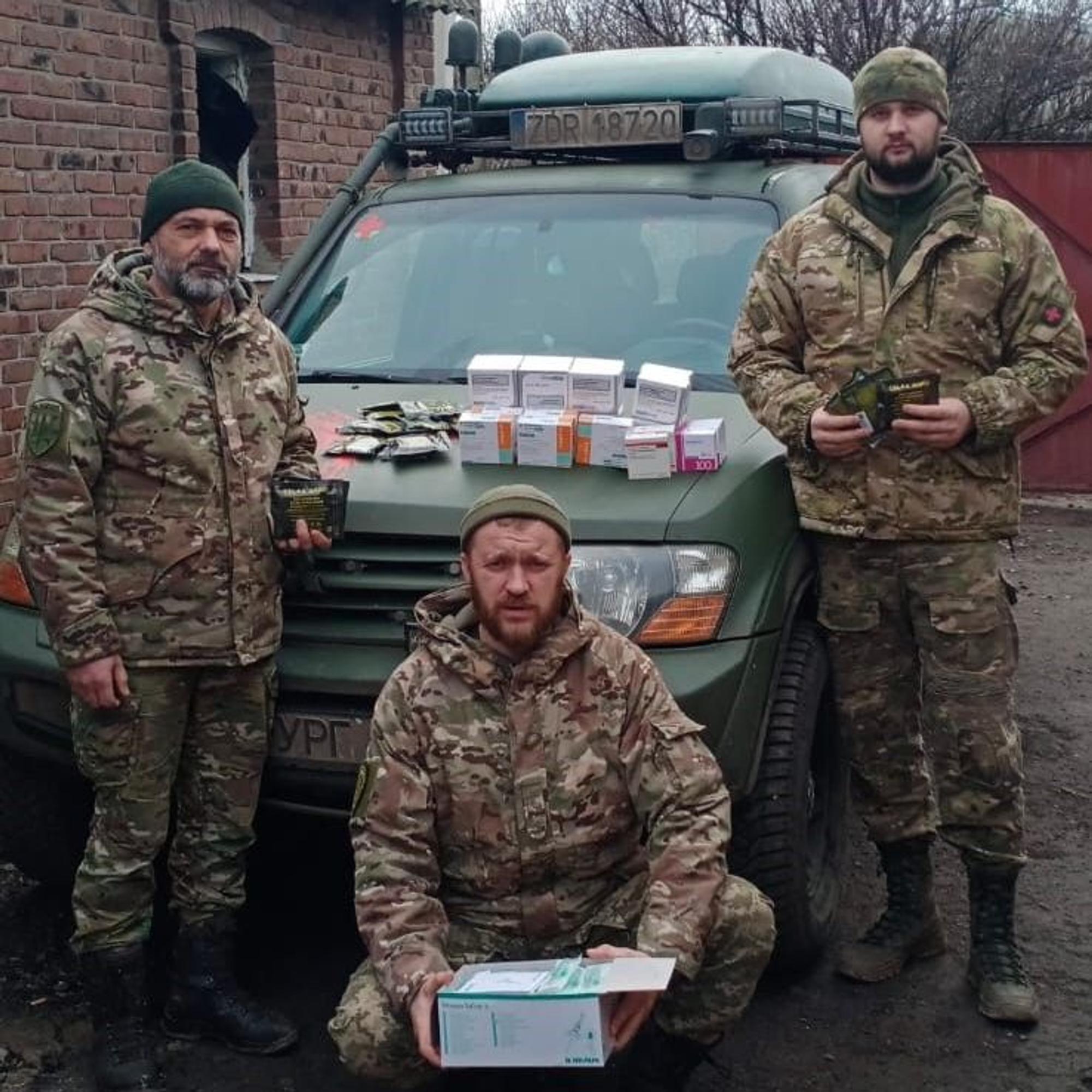 Drei ukrainische Soldaten stehen an einem Geländewagen. Sieh halten Medikamentenschachteln in den Händen.