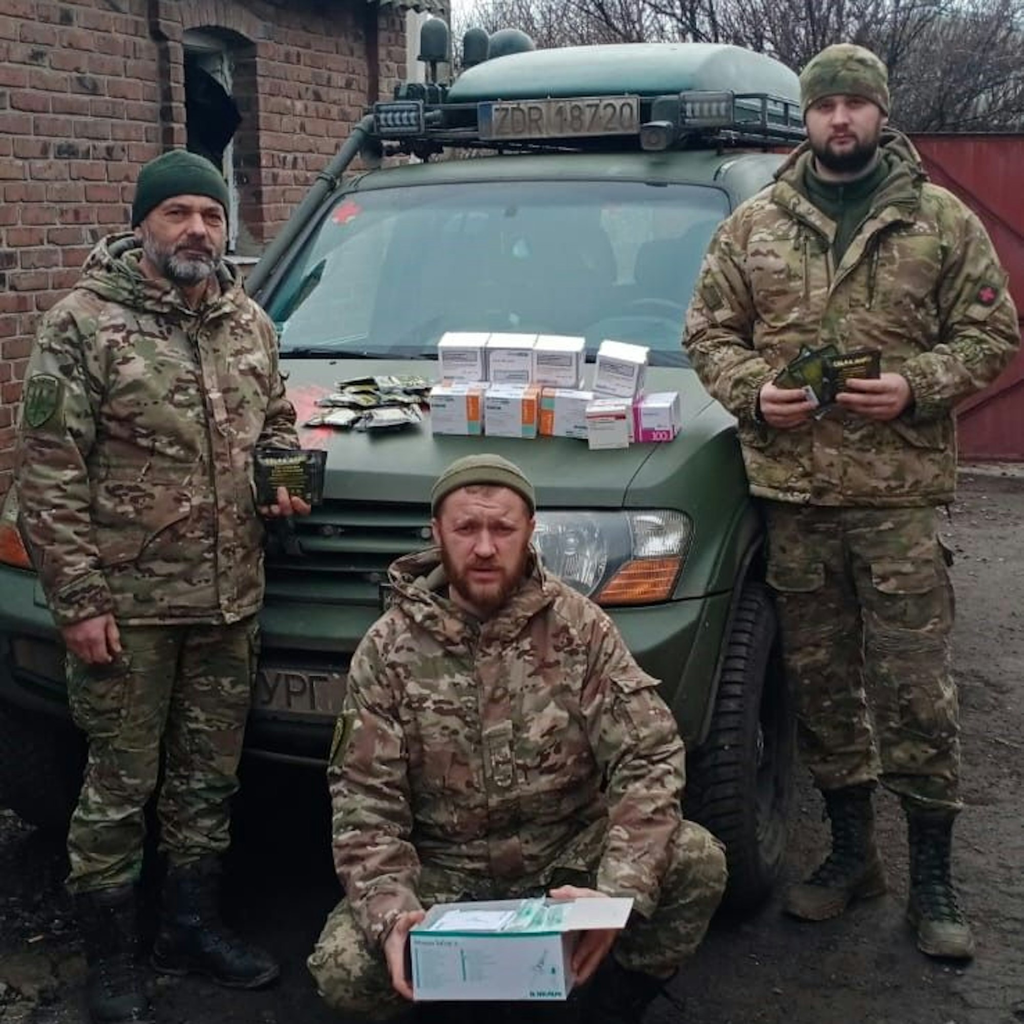 Drei ukrainische Soldaten stehen an einem Geländewagen. Sieh halten Medikamentenschachteln in den Händen.