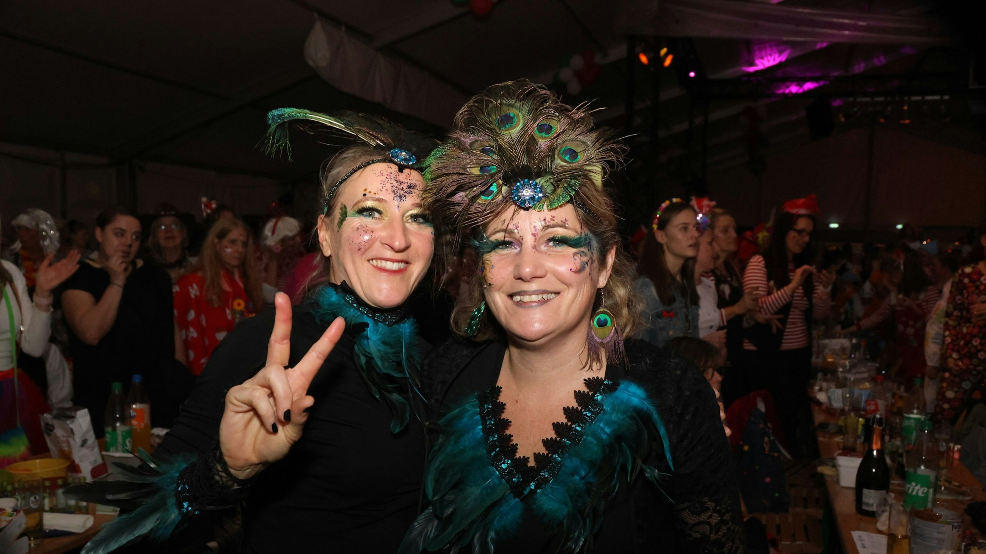 Zwei Frauen in schwarz-türkisen Kostümen schauen lachend in die Kamera.