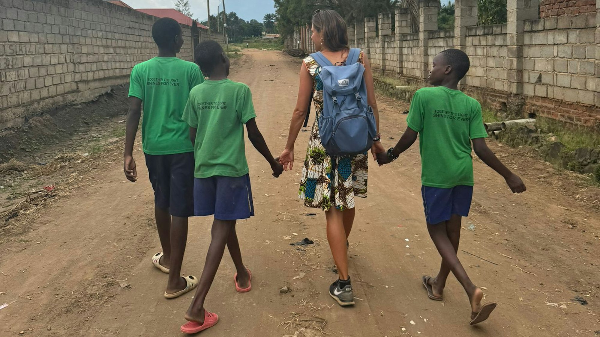 Eine Frau in Sommerkleid geht mit drei Kindern spazieren.