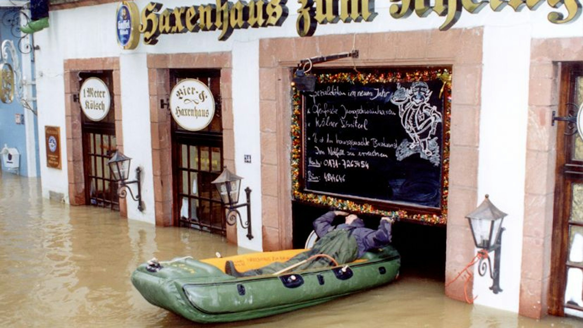 Ein Mann im Schlauchboot fährt durch die Tür eines vom Hochwasser überfluteten Hauses in der Kölner Altstadt.