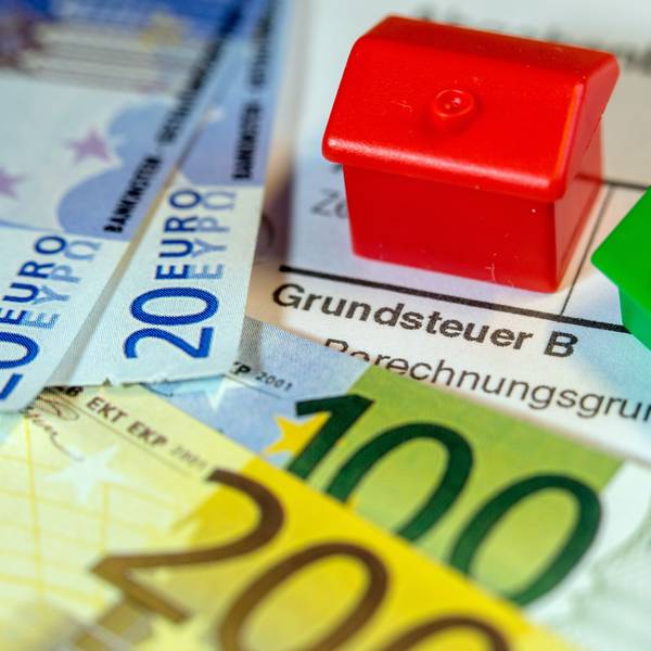 Ein Spielzeughaus und die Nachbildung von Euro-Geldscheinen liegen auf einem Abgabenbescheid für die Entrichtung der Grundsteuer.