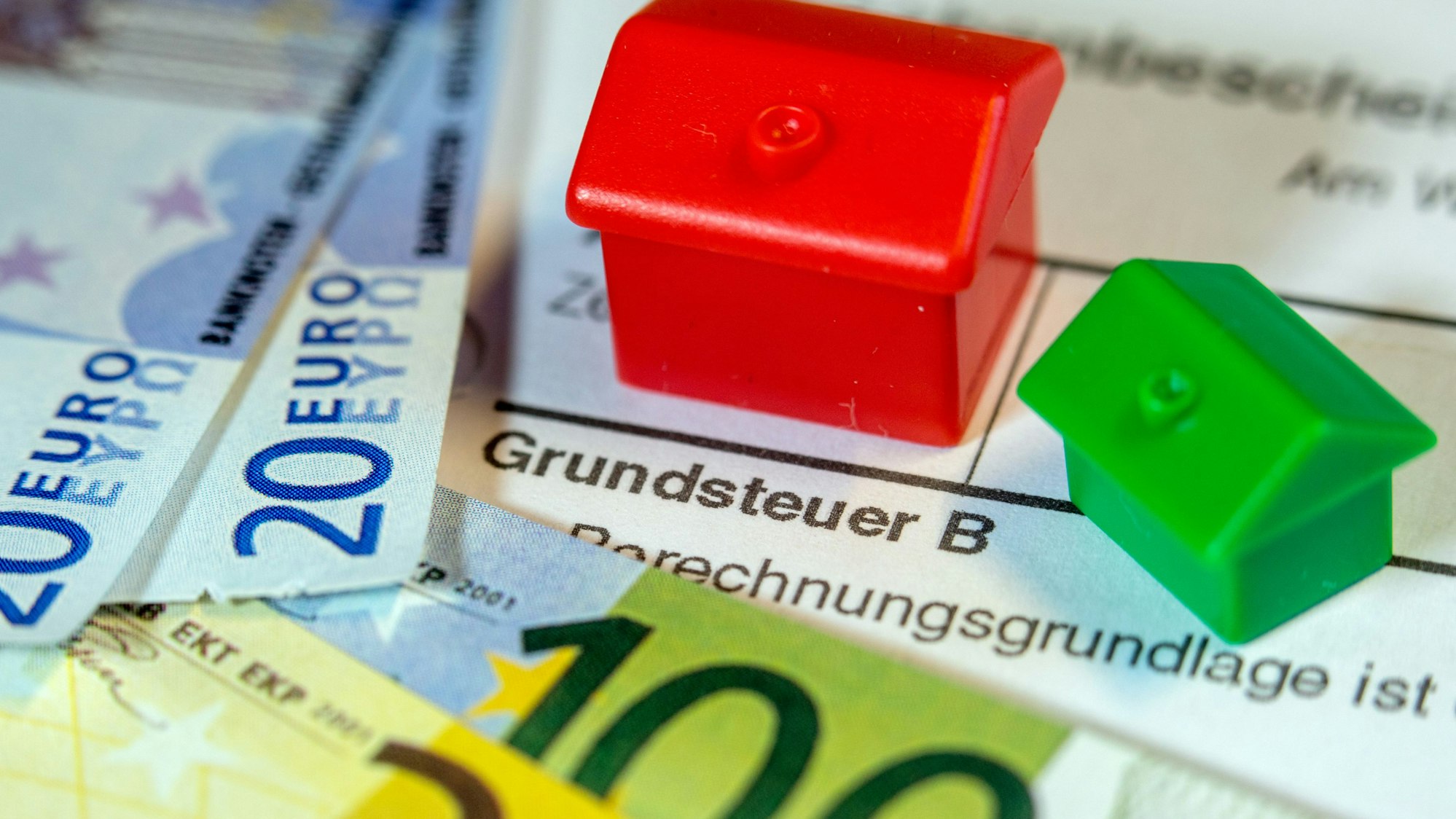 Ein Spielzeughaus und die Nachbildung von Euro-Geldscheinen liegen auf einem Abgabenbescheid für die Entrichtung der Grundsteuer.