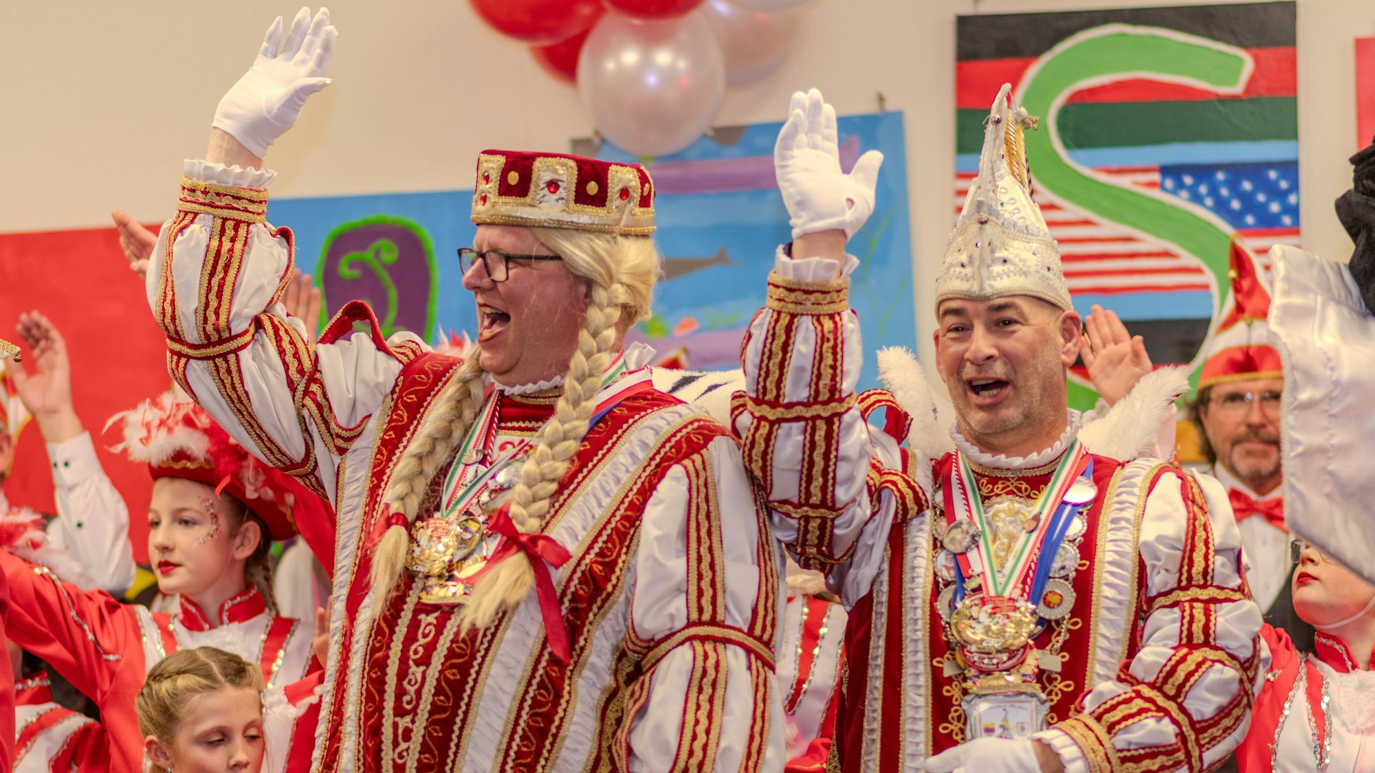 Zwei Männer in rot-weißen Karnevalskostümen winken und lachen.