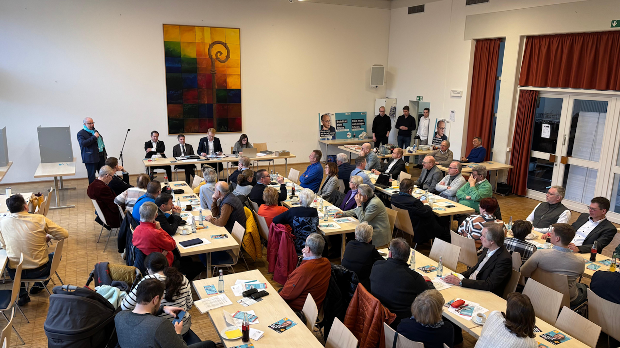 In einem Saal sitzen Frauen und Männer an Tischen.