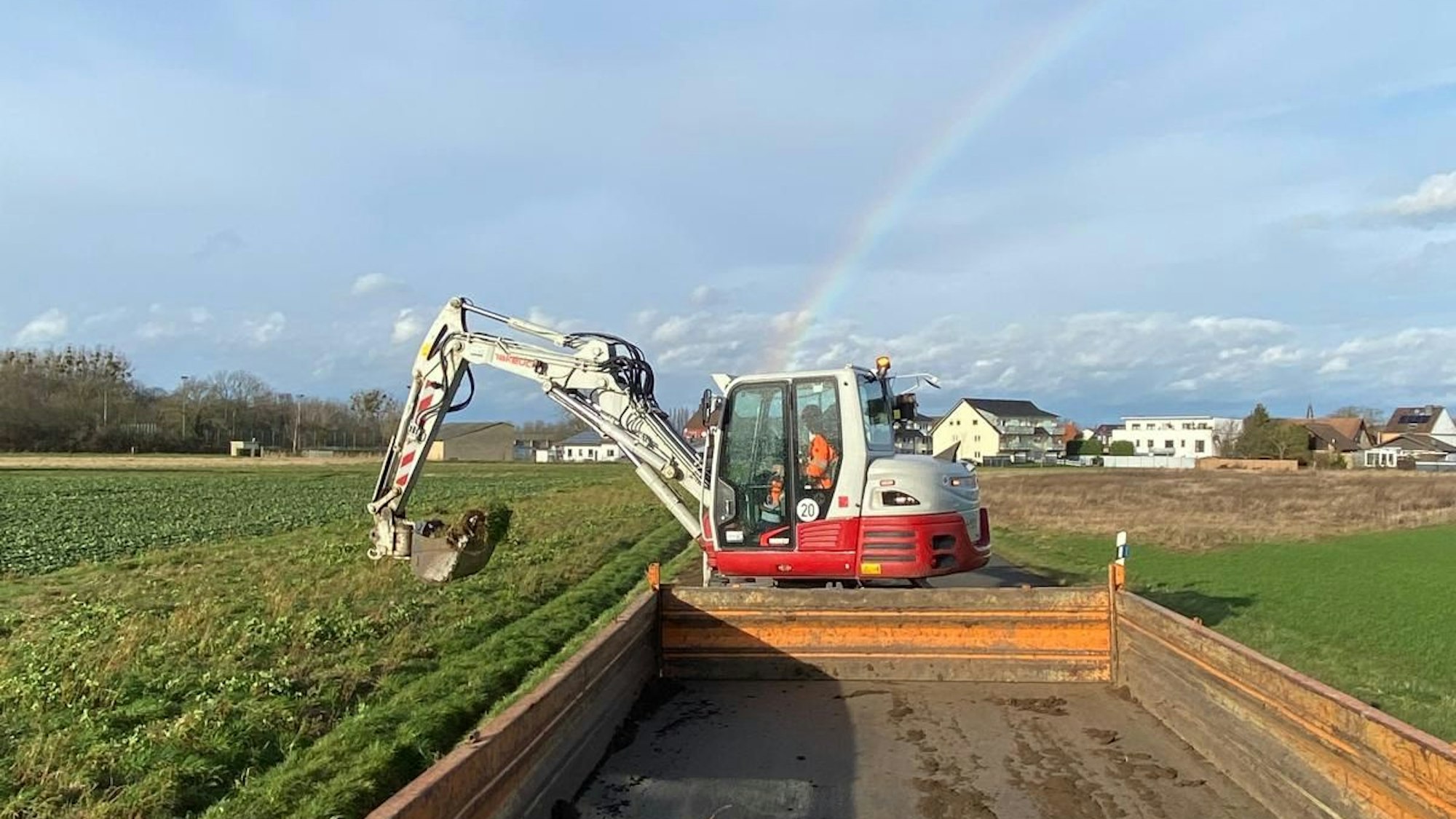 Ein Bagger gräbt einen Graben neben einem Feldweg aus.