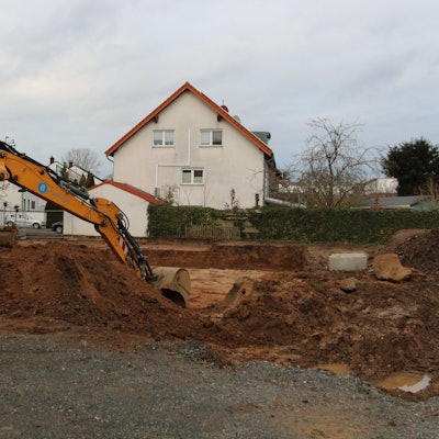 Eine Baggerschaufel gräbt sich durch das Erdreich.