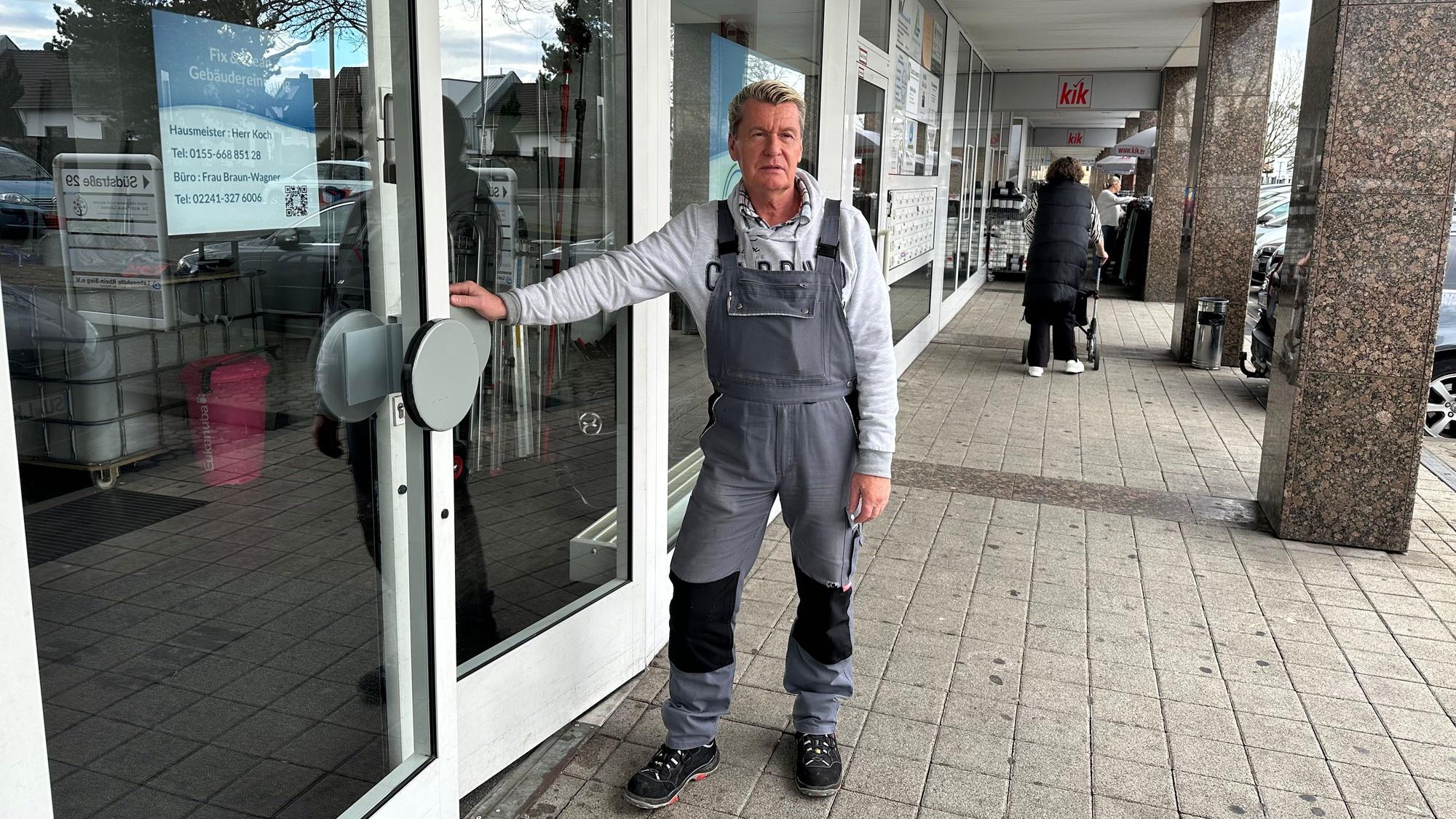 Helmut Koch ist seit neun Jahren Hausmeister in den Südarkaden in Sankt Augustin. Er steht an der Türe zu seinem Büro mit einem Montaganzug.