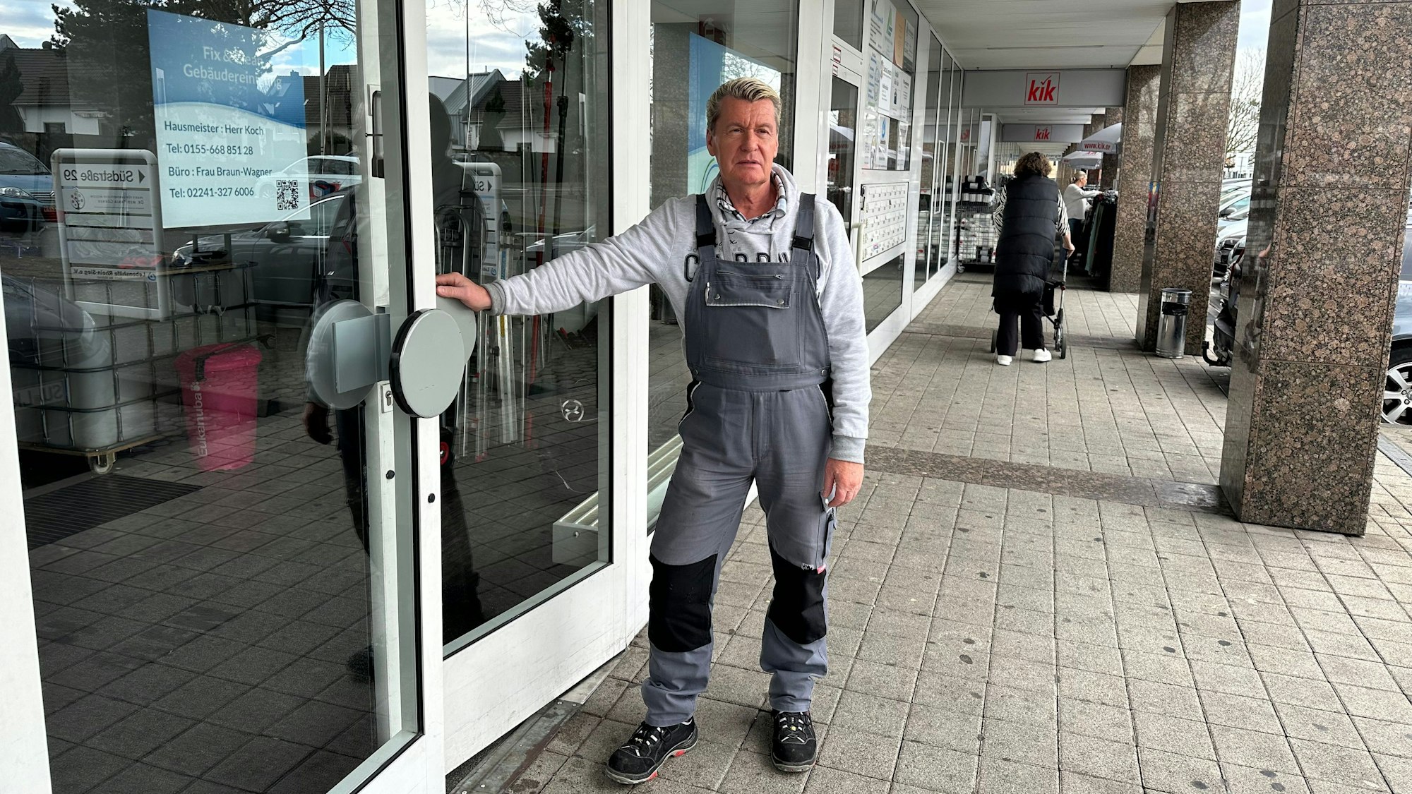 Helmut Koch ist seit neun Jahren Hausmeister in den Südarkaden in Sankt Augustin. Er steht an der Türe zu seinem Büro mit einem Montaganzug.