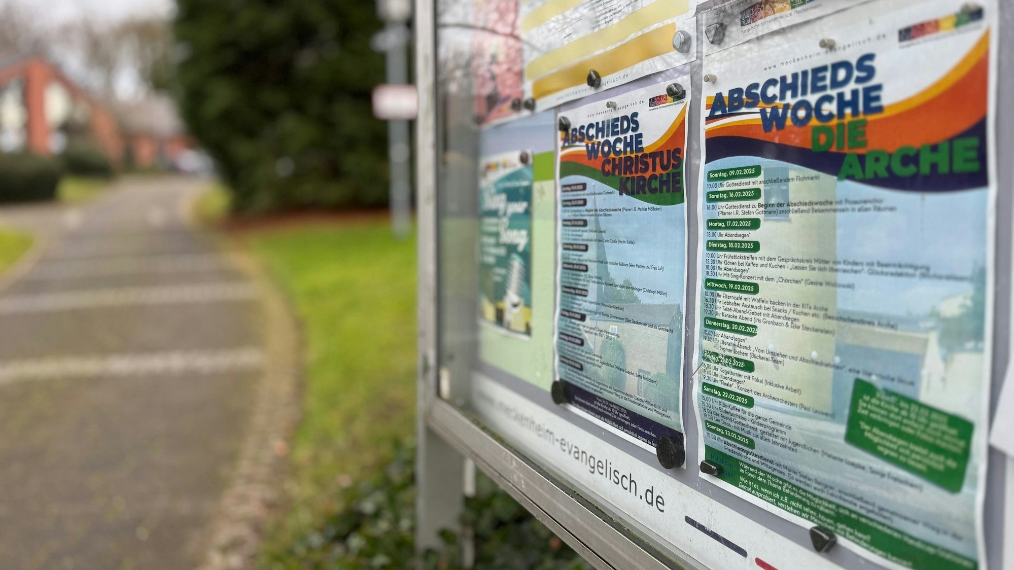 Im Vordergrund der Schaukasten, im Hintergrund das Gebäude der Kirche.