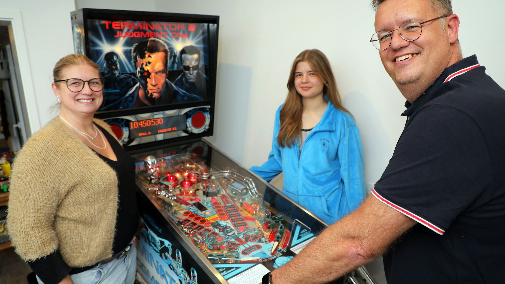 Michael Schlaeger steht mit seiner Frau Yvonne und Tochter Julia an einem Flipper.