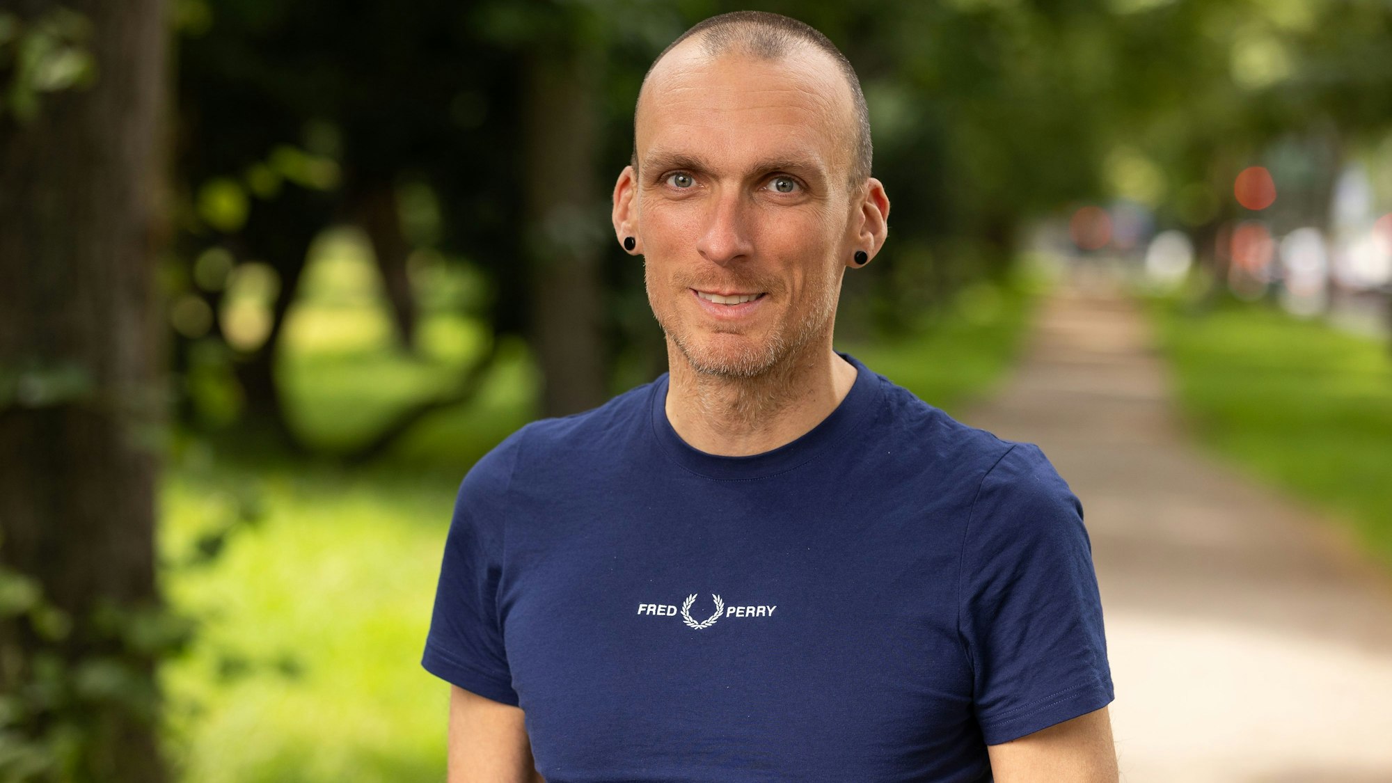 Auf dem Bild ist der Referent in einem blauen T-Shirt in einem Park zu sehen.