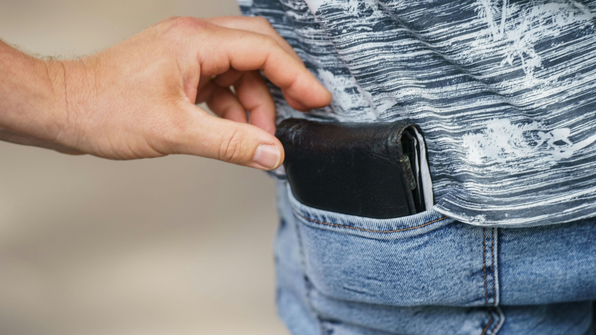 Der Diebstahl einer Geldbörse wird im Hauptbahnhof demonstriert. Die Hand eines Mannes greift nach einem Portemonnaie in der Gesäßtasche einer Hose.