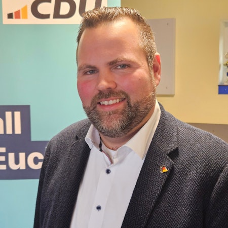 Michael Kehren steht vor einem CDU-Roll-up. Er trägt einen sauber gestutzten Bart, Sakko und ein weißes Hemd.