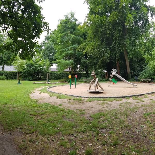 Zu sehen ist ein Spielplatz in einem grünen Park.