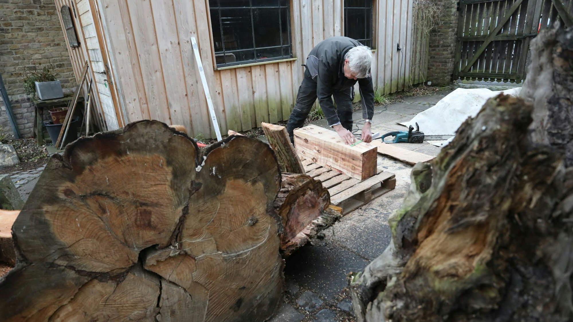 Ein Mann misst an einem rechteckigen Holzstück, das er aus einem Stamm gesägt hat.