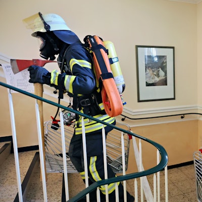 Das Bild zeigt zwei Feuerwehrleute bei einer Übung. Sie befinden sich gerade in einem Treppenhaus.