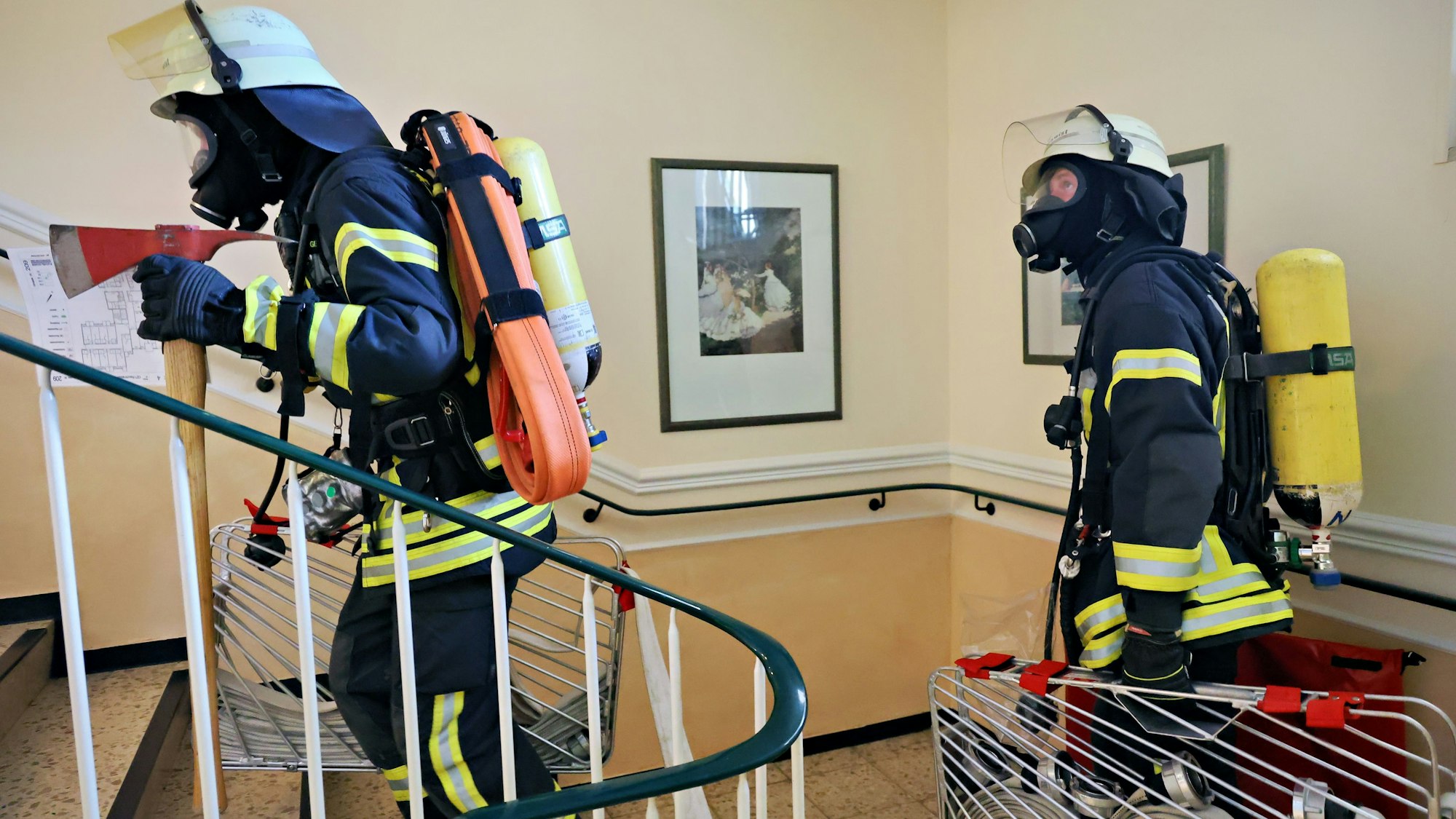 Das Bild zeigt zwei Feuerwehrleute bei einer Übung. Sie befinden sich gerade in einem Treppenhaus.