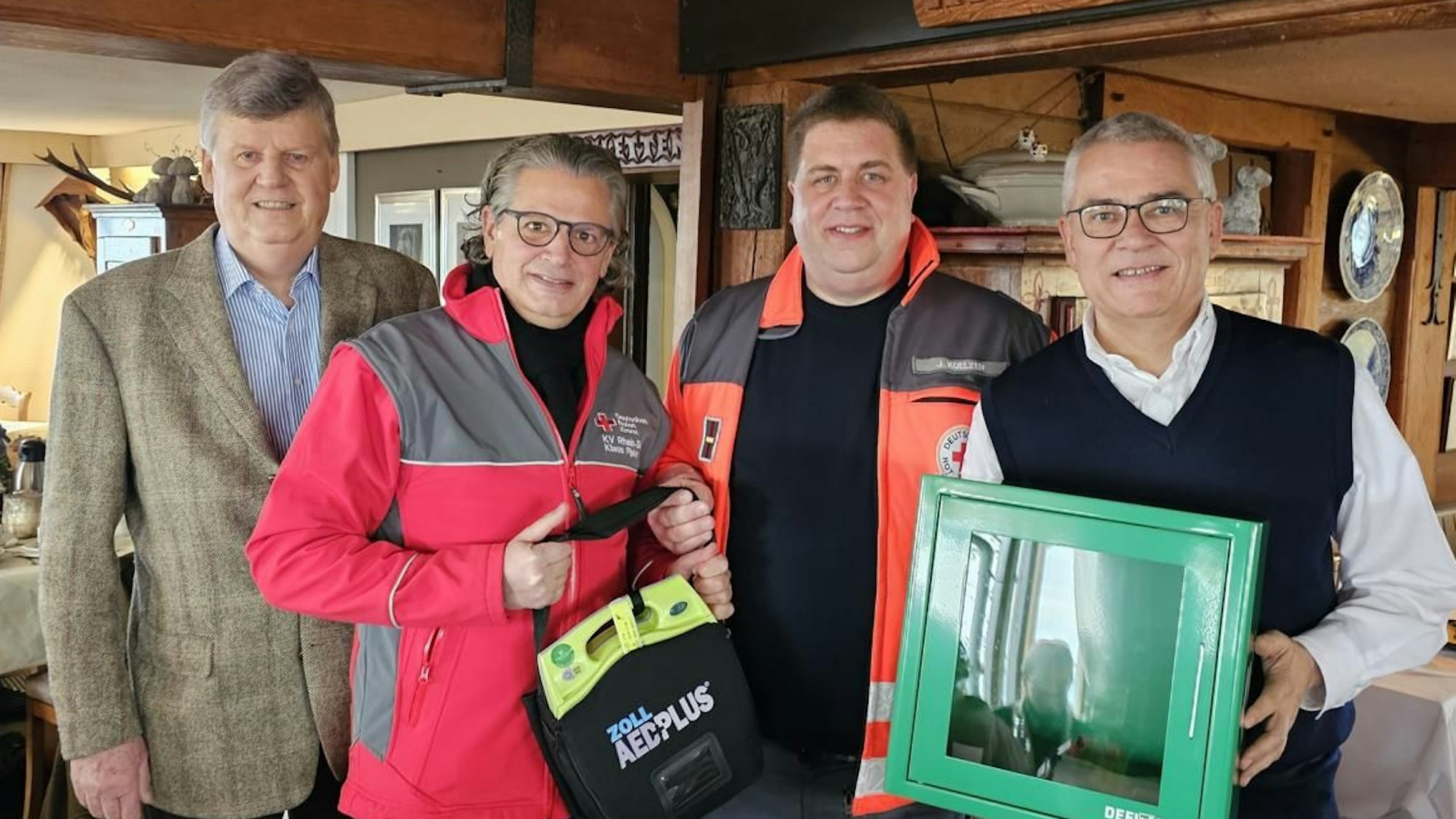 Vier Männer stehen nebeneinander, einer hält einen Defibrillator in der Hand.