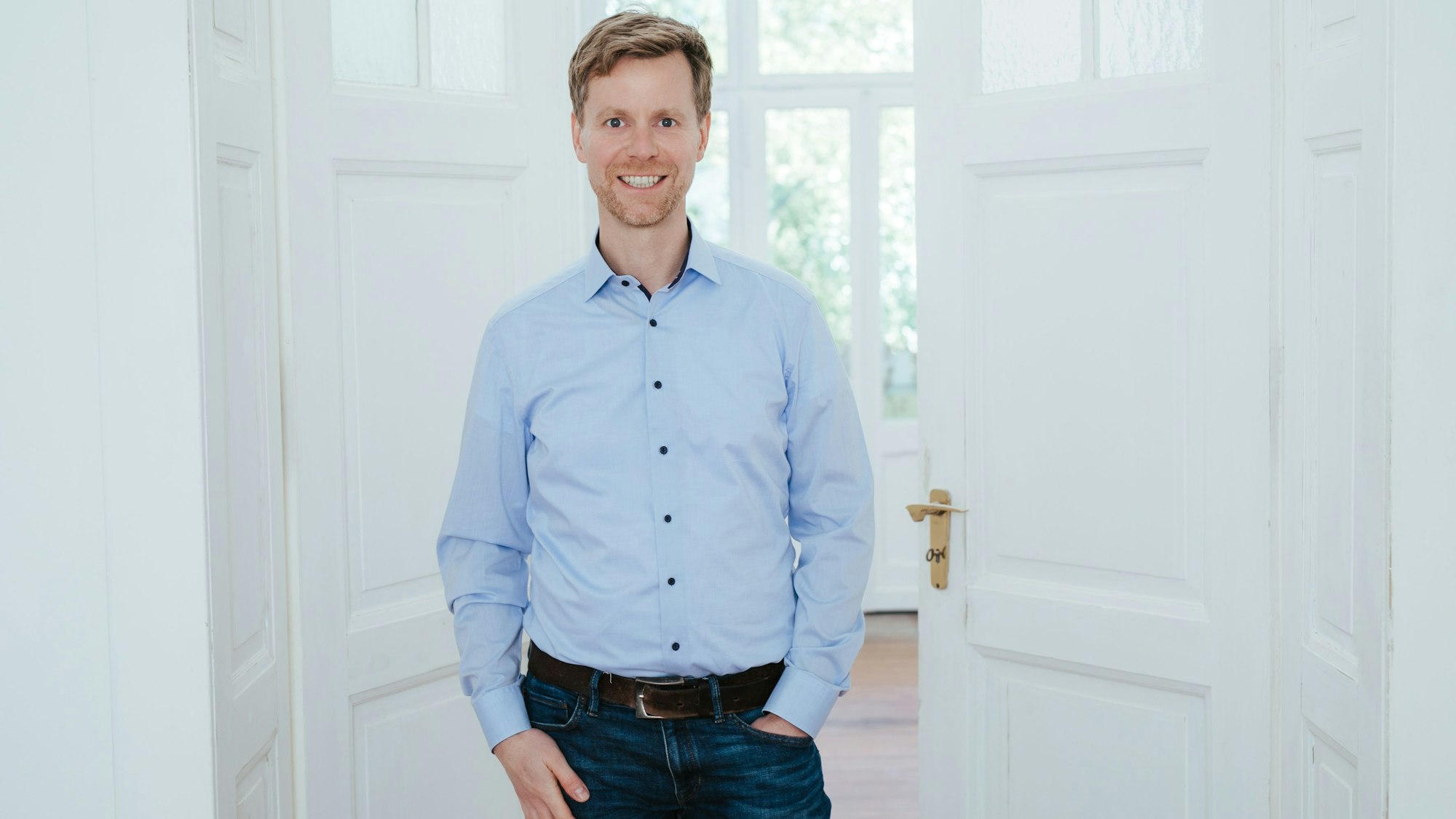 Ein Mann in blauem Hemd vor einer weißen, halb geöffneten Tür.