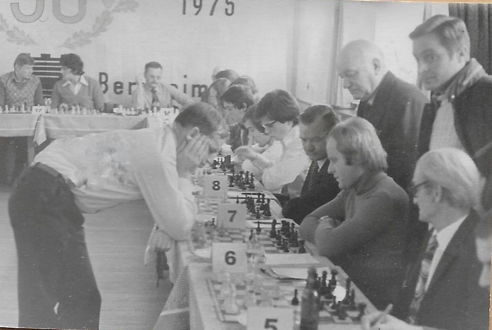 Eine ganze Tischreihe mit Schachbrettern ist zu sehen, an jedem Brett jeweils ein Gegner für Großmeister Wolfgang Unzicker. Der steht über einem der Bretter gebeugt und denkt über den nächsten Zug nach.