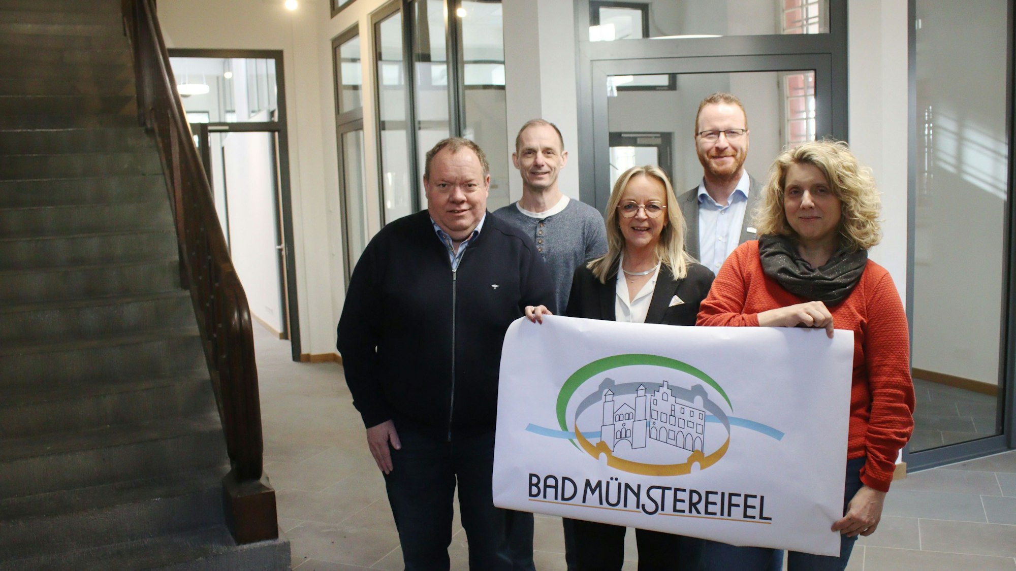 Die Verantwortlichen der Stadt Bad Münstereifel stehen im frisch renovierten Erdgeschoss und halten ein Plakat mit dem Logo der Stadt in die Höhe.