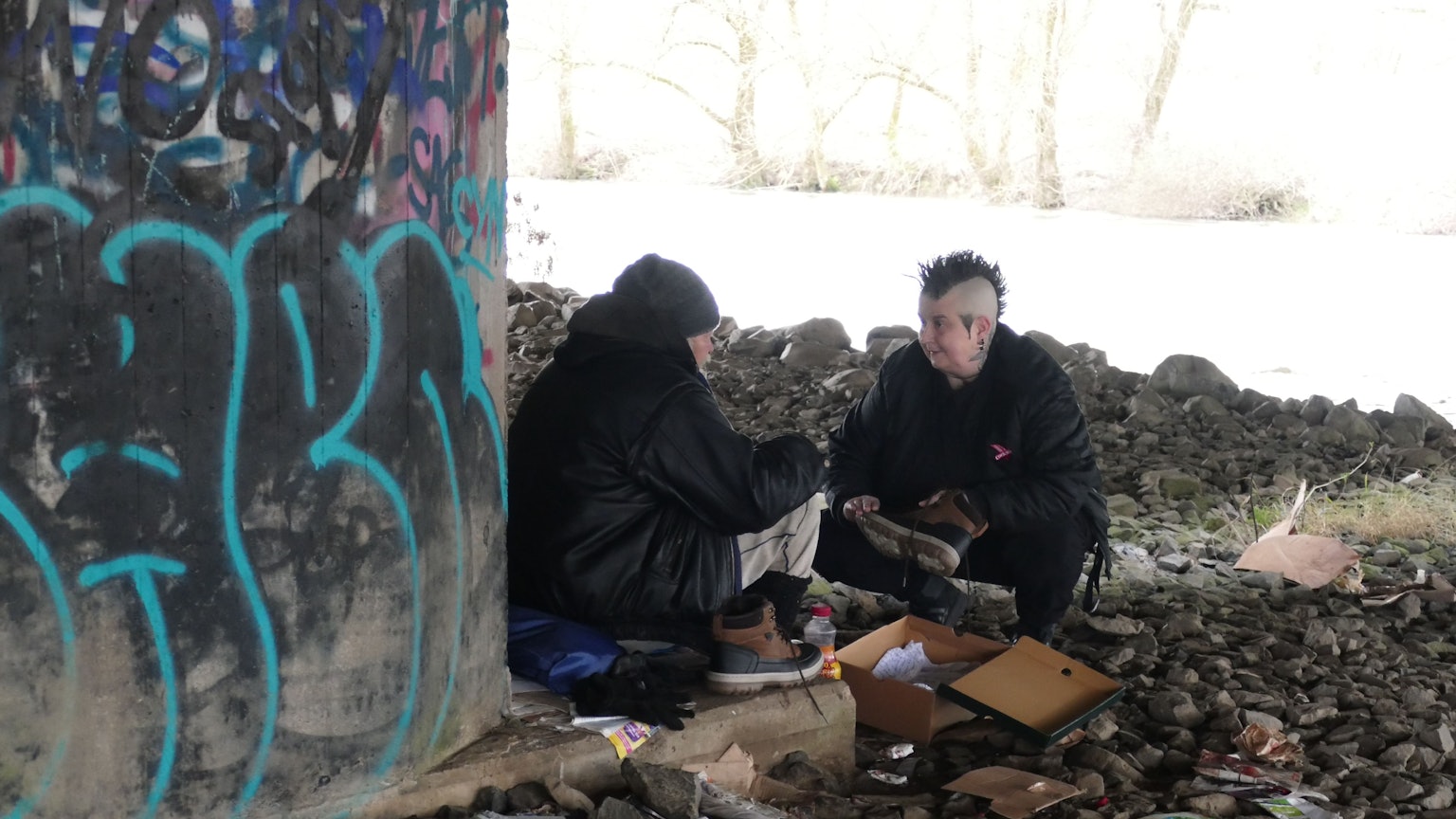 Varressa Lombardi-Boccia sitzt einem obdachlosen Mann gegenüber, der aus dieser Perspektive nicht zu erkennen ist.