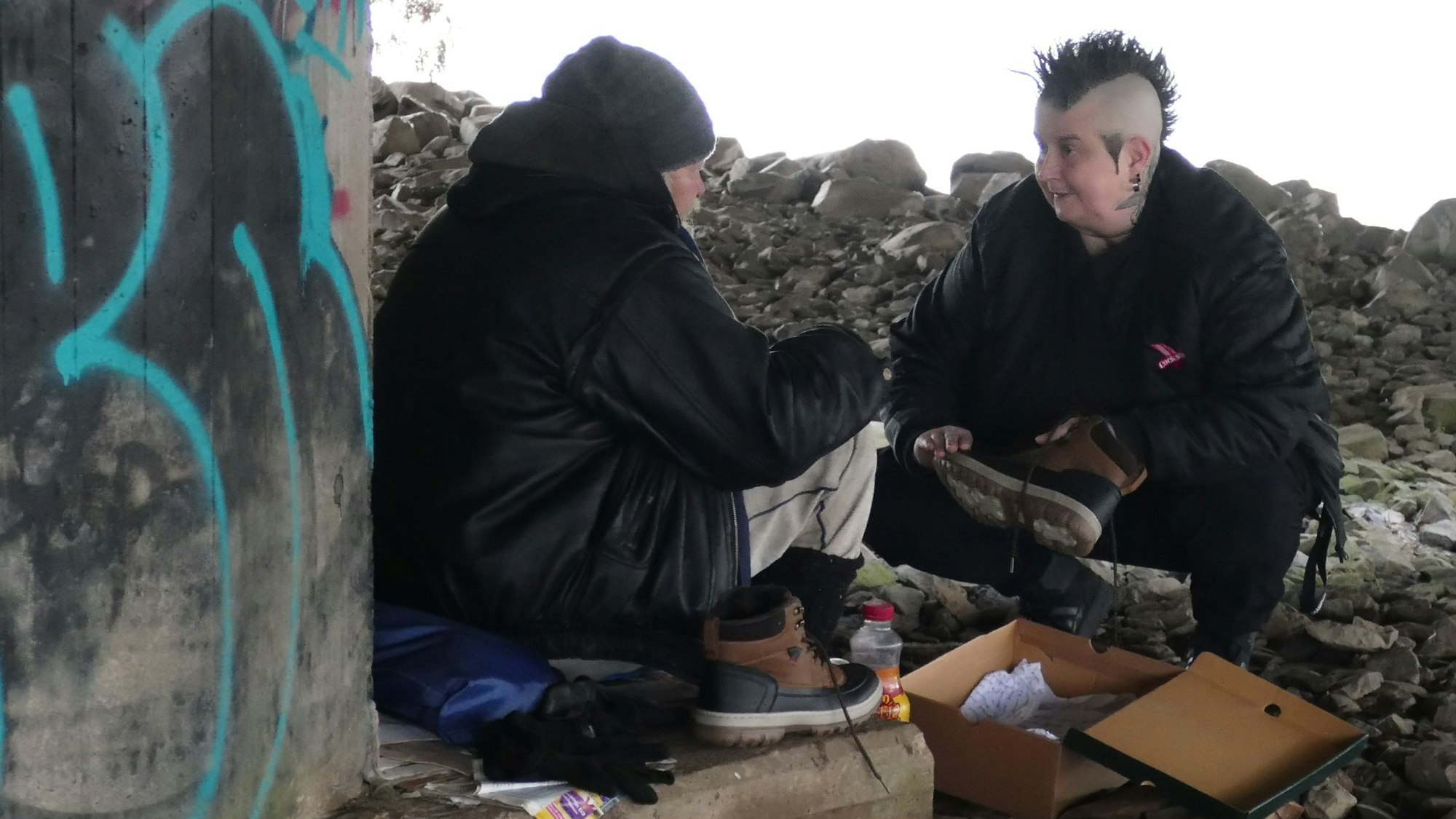 Varressa Lombardi-Boccia sitzt einem obdachlosen Mann gegenüber, der aus dieser Perspektive nicht zu erkennen ist.