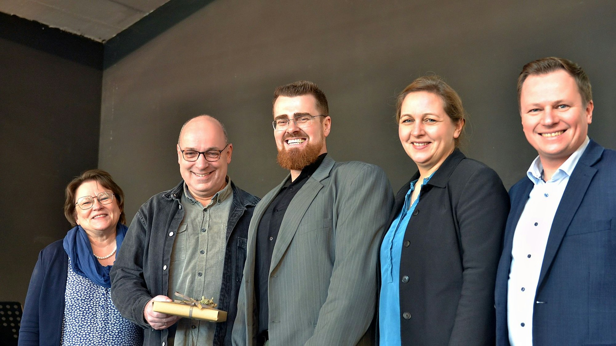 Zwei Frauen und drei Männer stehen in einer Reihe nebeneinander und lachen in die Kamera.