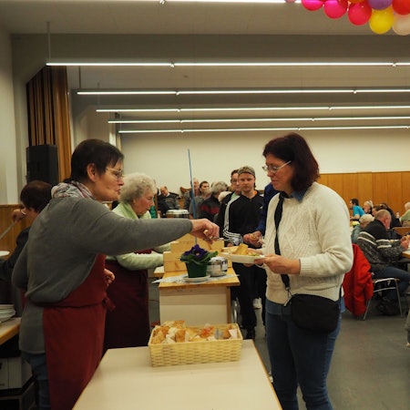 Helferinnen geben die Suppe aus. Eine Reihe von Gästen steht an. Die Tische im Raum sind gut gefüllt.