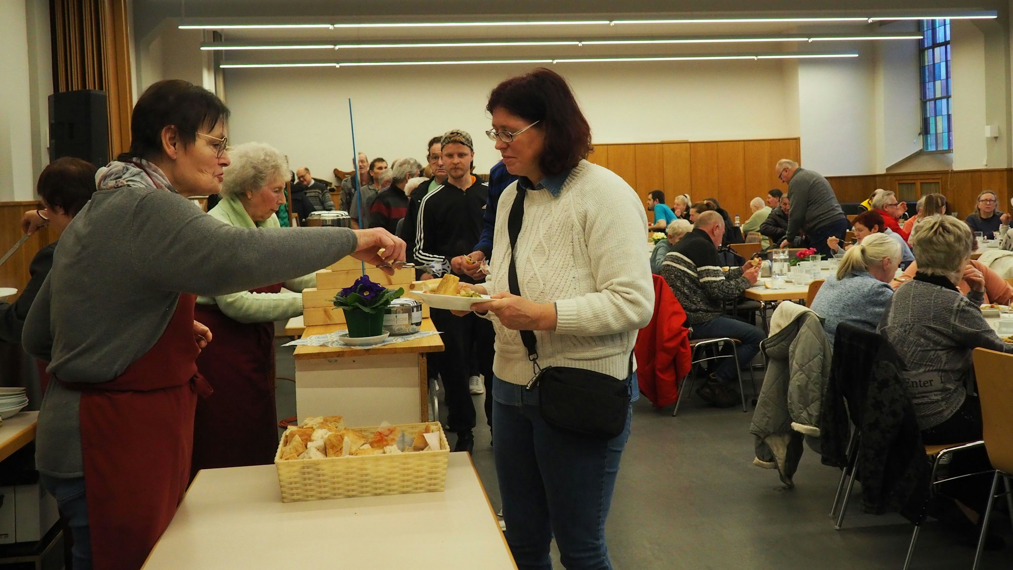 Helferinnen geben die Suppe aus. Eine Reihe von Gästen steht an. Die Tische im Raum sind gut gefüllt.