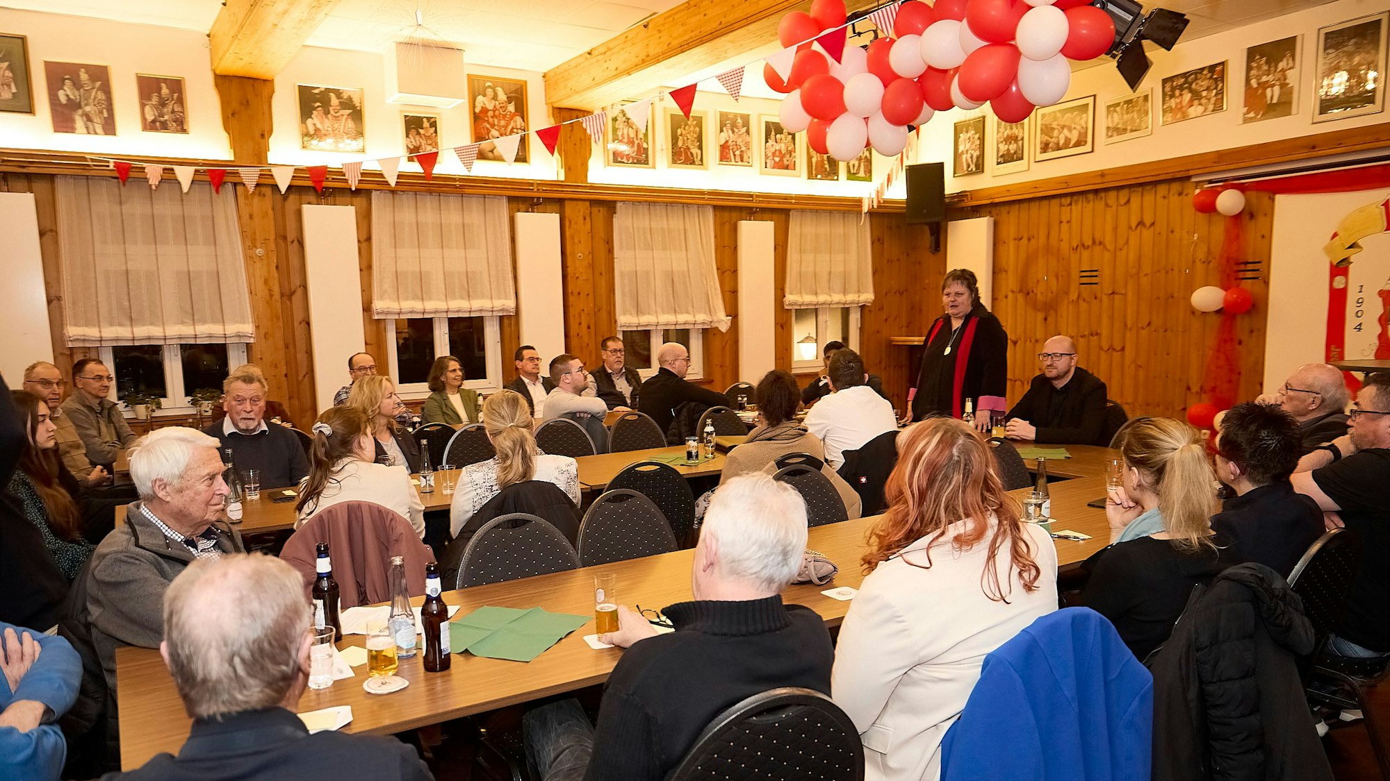 Frauen und Männer sitzen an Tischen, sie hören einer Rednerin zu, die als Einzige steht.