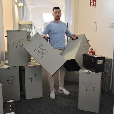 Ein Mann steht zwischen zahlreichen Wahlurnen.