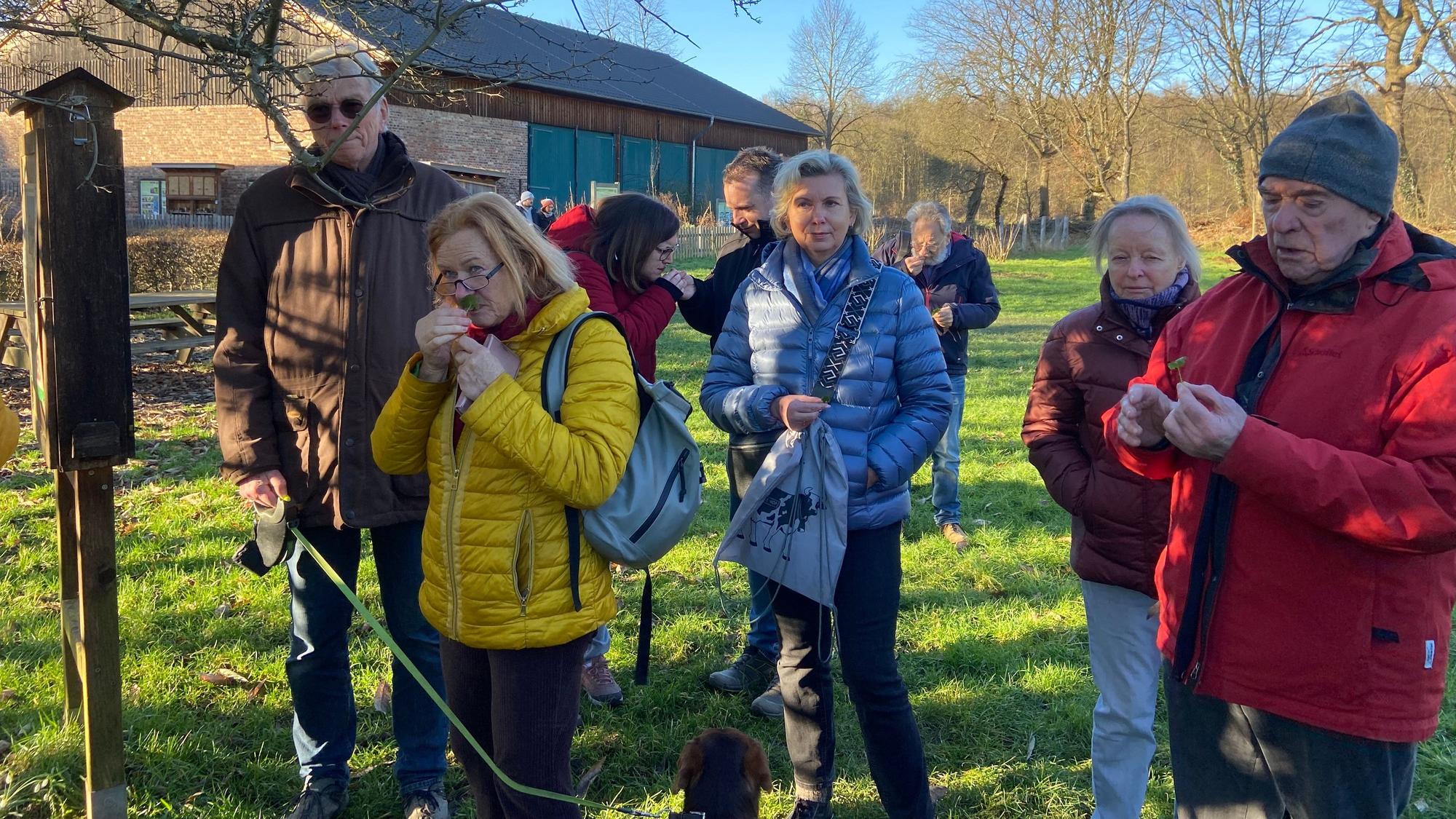 Menschen in bunten Anoraks stehen auf einer Wiese, sie haben Kräuter in der Hand.